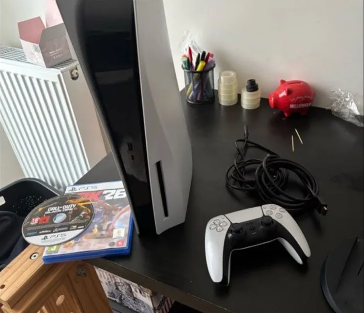 The seller's own photo: a PS5, its controller, cables and two games on a cluttered desk.